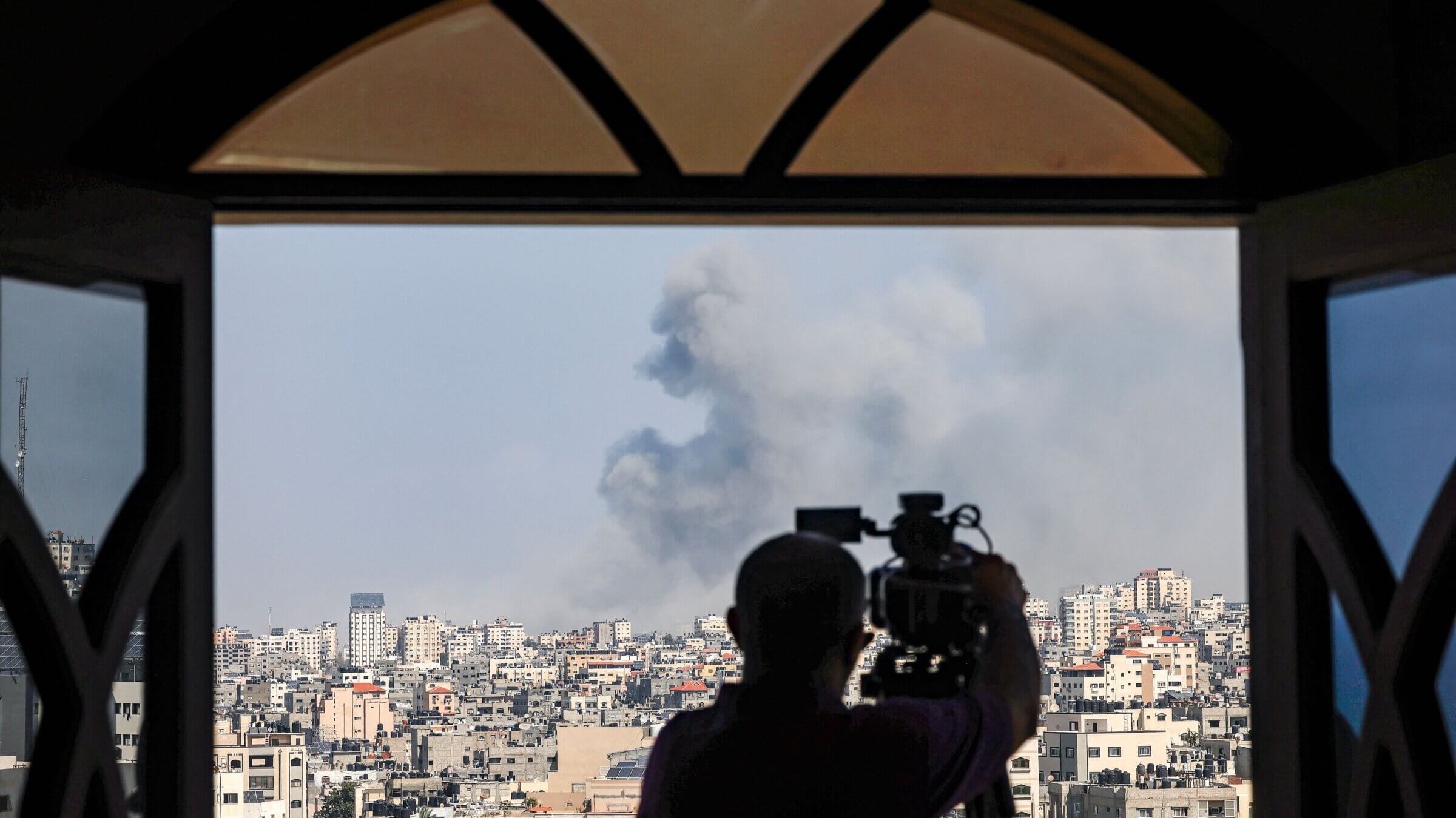 A cameraman films while smoke plumes billow during Israeli air strikes in Gaza City Thursday. Palestinian Americans are watching the conflict unfold with mounting dread, as the U.S. government has thrown its weight behind Israeli military action.