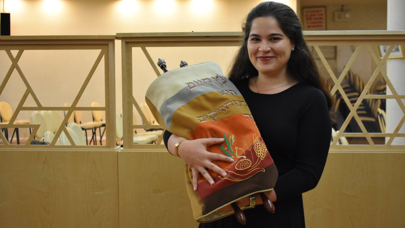 An Orthodox woman holding a Torah scroll in a synagogue.