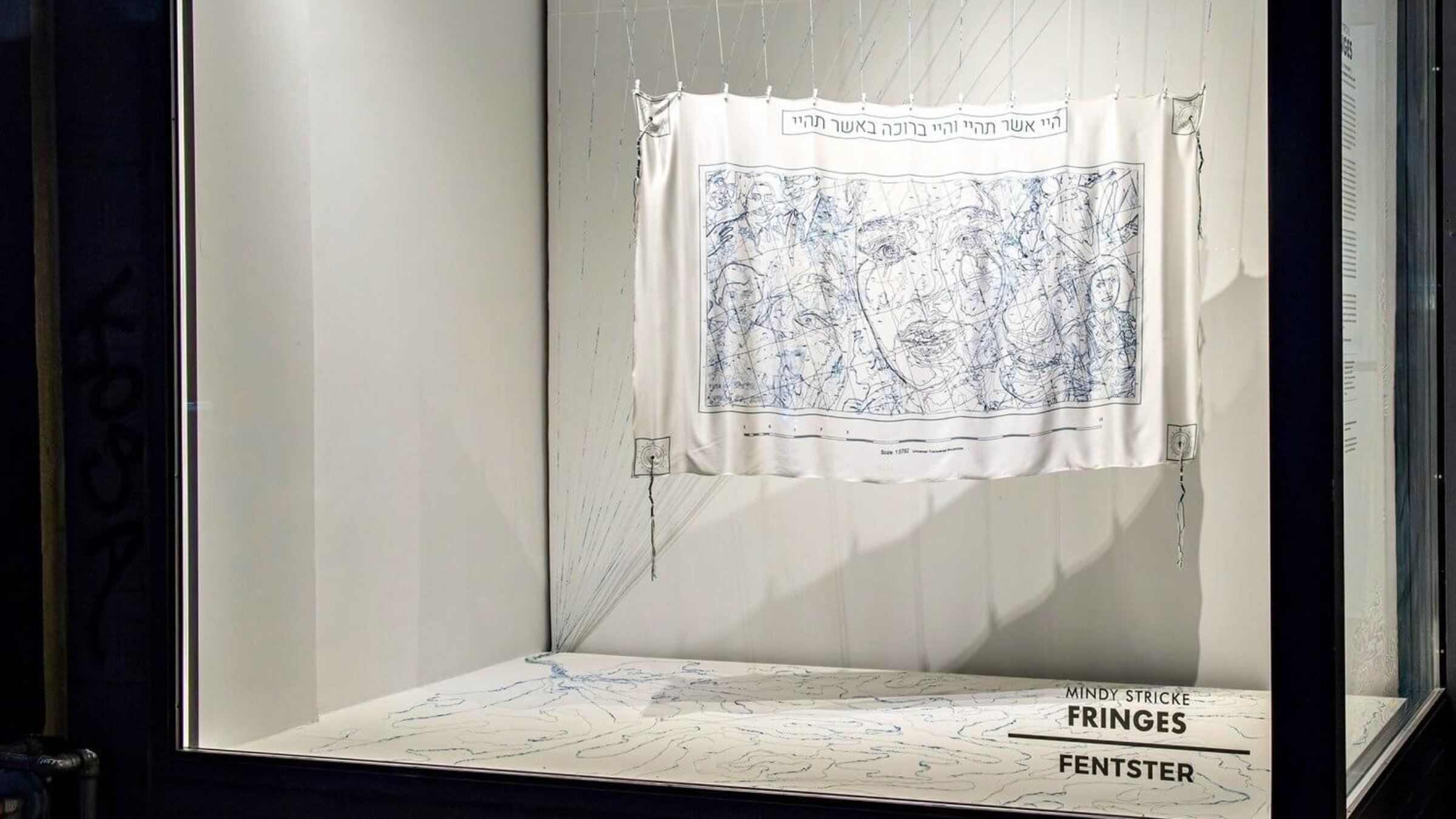 The tallit, installed in Fentster's window, creates another map with the fringes dangling onto the floor.