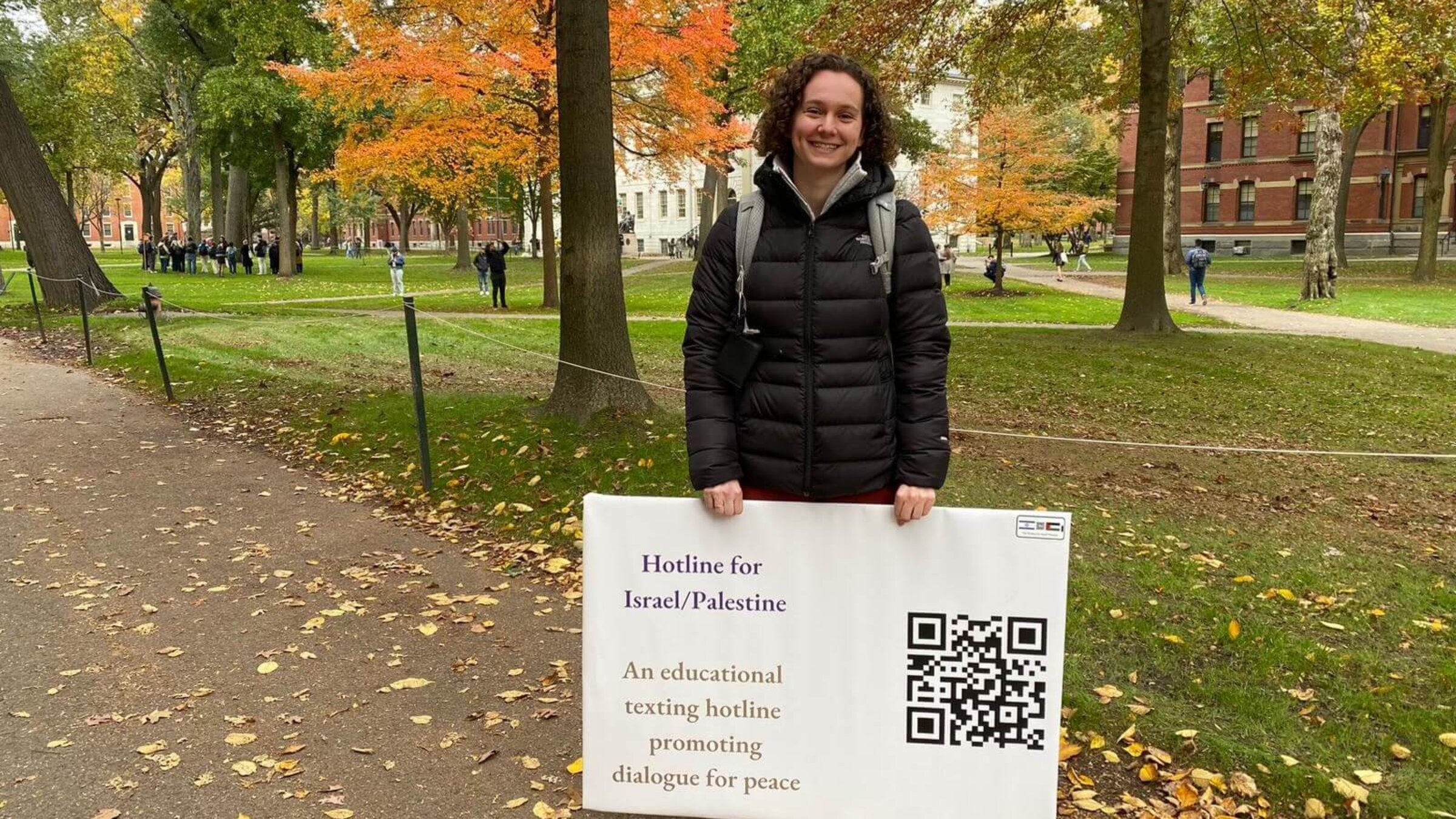 Shira Hoffer in Harvard Yard with a sign for her hotline providing resources and information about the Israeli-Palestinian conflict.