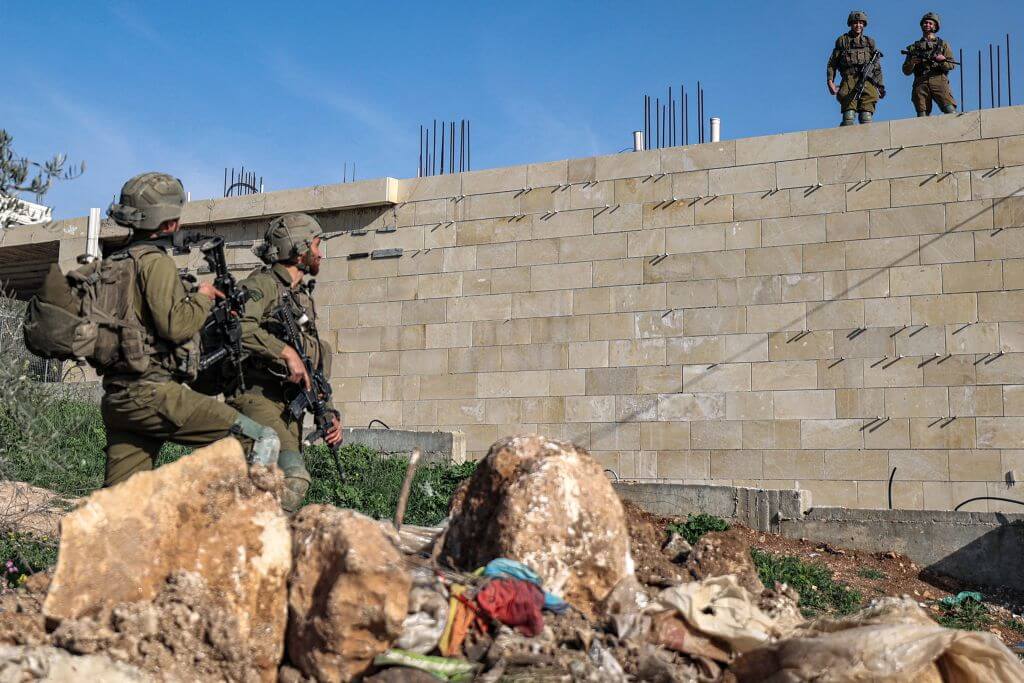 Israeli soldiers stationed atop a building speak with others positioned on the ground in the Palestinian town of Huwara near Nablus in the occupied West Bank on February 27, 2023. 