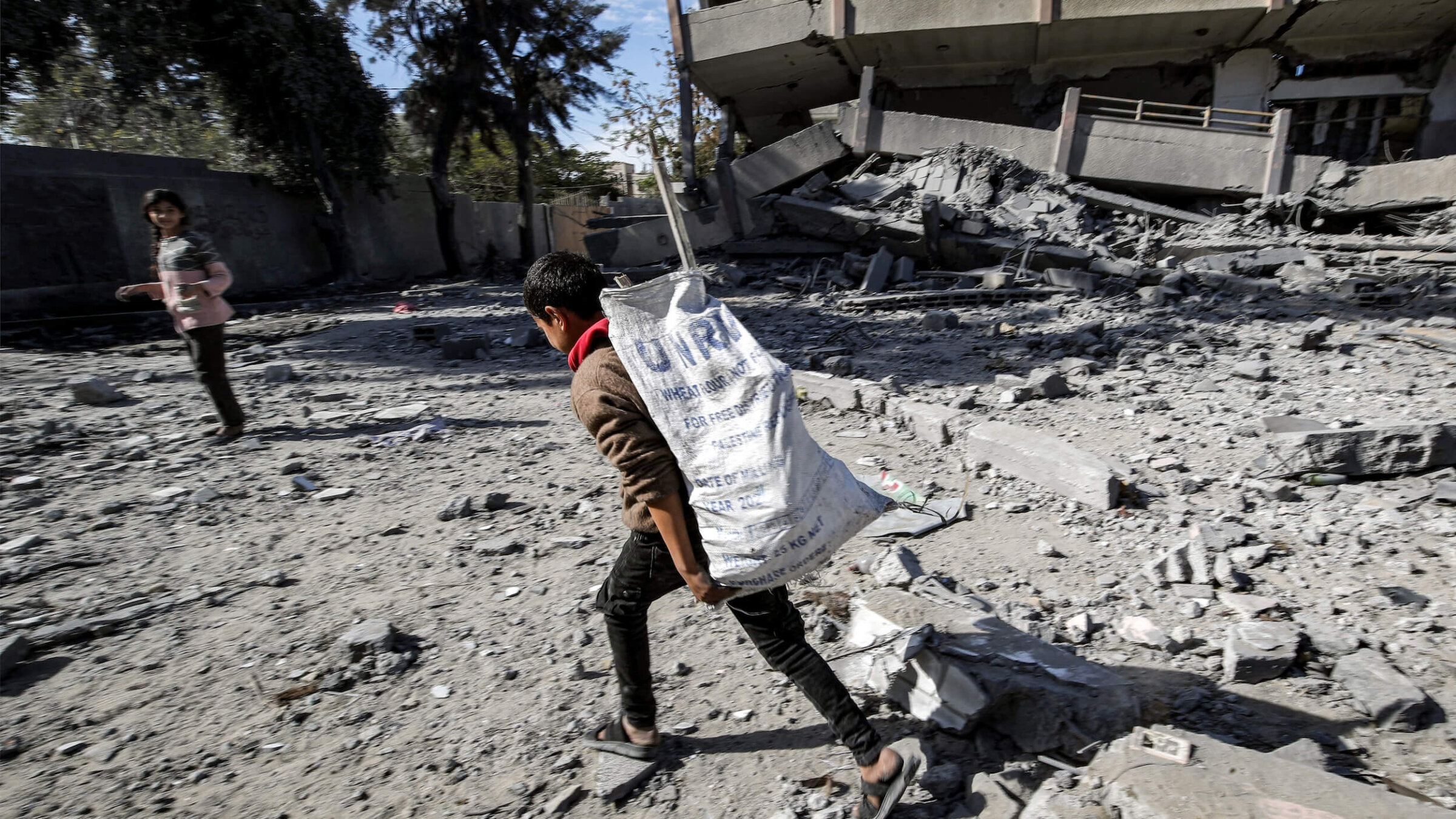 A boy carries a sack bearing the logo of the United Nations Relief and Works Agency for Palestine Refugees in the Near East (UNRWA), filled with salvaged items from the rubble of a destroyed high school in the Nuseirat camp for Palestinian refugees, which was severely damaged by Israeli bombardment on Feb. 1.