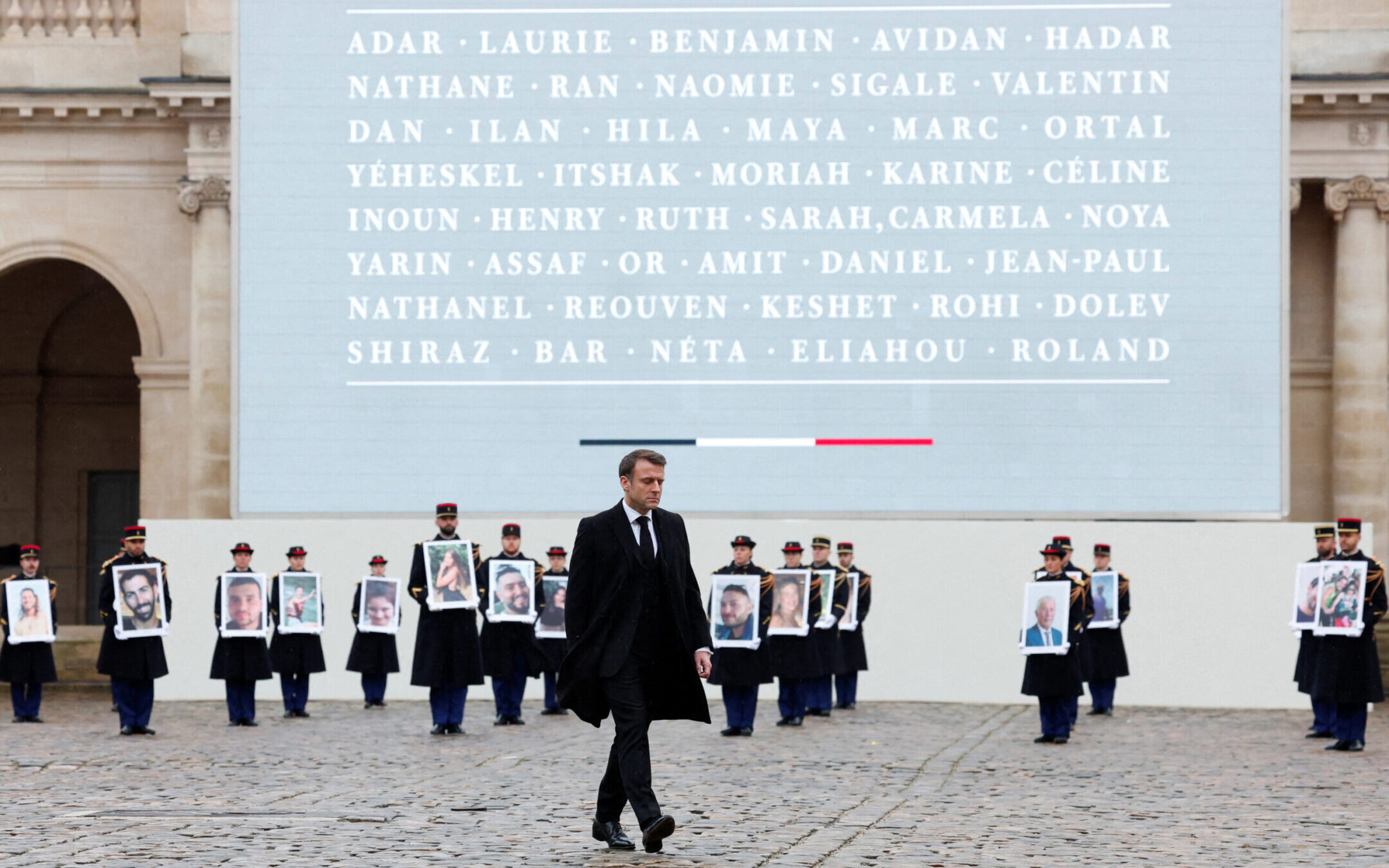 French President Emmanuel Macron walks in front of members of the French Republican Guard holding portraits of the 42 French and French-Israeli citizens killed in Israel on Oct. 7, 2023, during a ceremony to pay tribute to the French victims of the attack by Hamas, at the Invalides memorial complex in Paris, Feb. 7, 2024. (Gonzalo Fuentes/AFP via Getty Images)