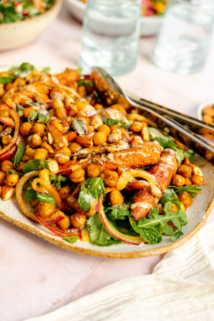 A salad of chickpeas, onions, carrots, and mint leaves, drizzled with tahini, on a long plate.