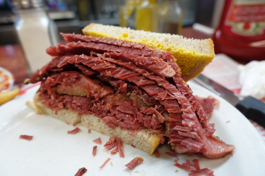 A cross section of a heaping sandwich with mustard on the interior of the bread slices and lots and lots of sliced red smoked meat.