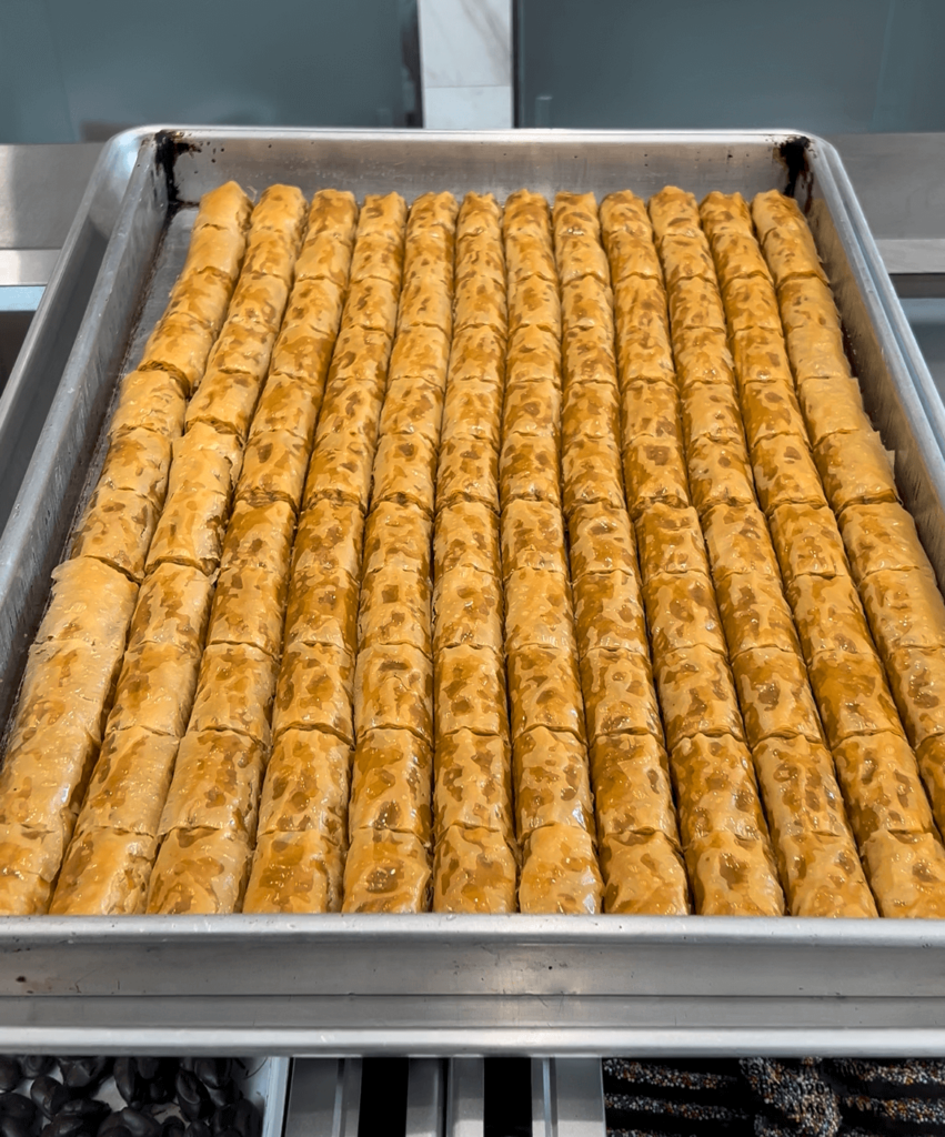 A tray of golden colored baklava cigars lined up vertically.