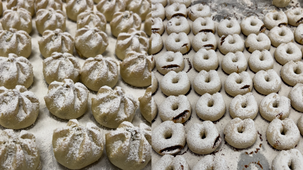 On the left, rows of spiral shaped cookies covered with powdered sugar. On the right, rows of donut-shaped cookies covered with powdered sugar and with some breaks that reveal dark-colored interiors.