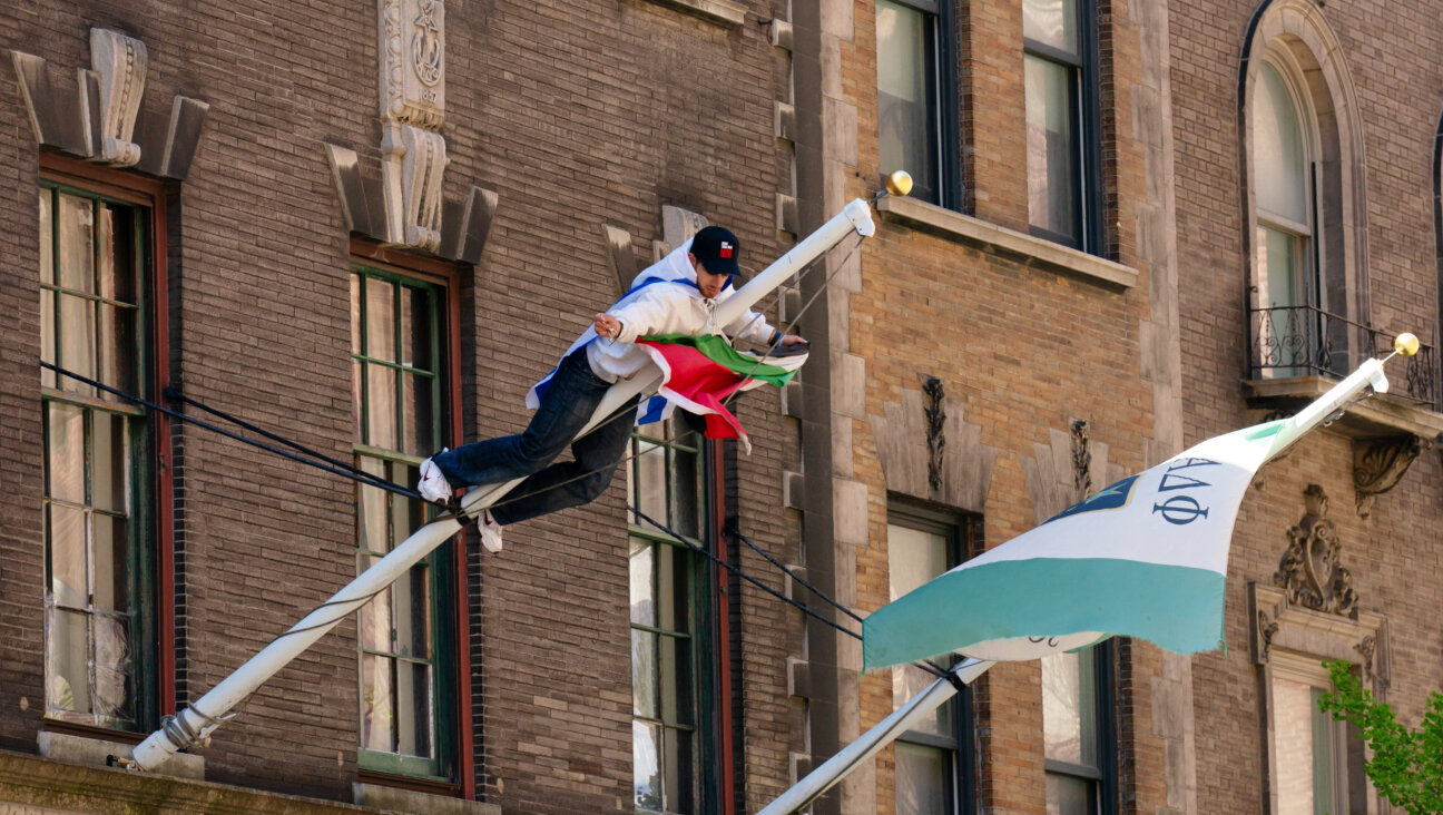 A man wearing an Israeli flag climbs a pole to remove a Palestinian flag from a Columbia University fraternity building on April 26, 2024 in New York City