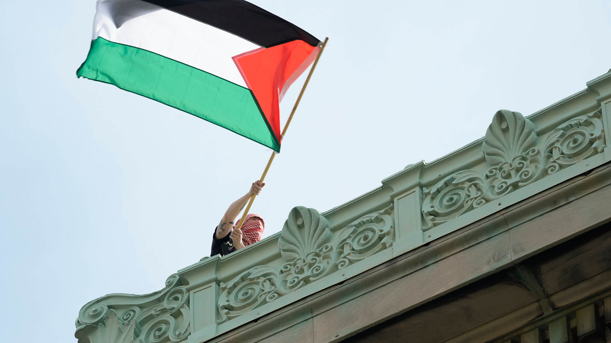A student protester waves a Palestinian flag above Hamilton Hall  on the campus of Columbia University.