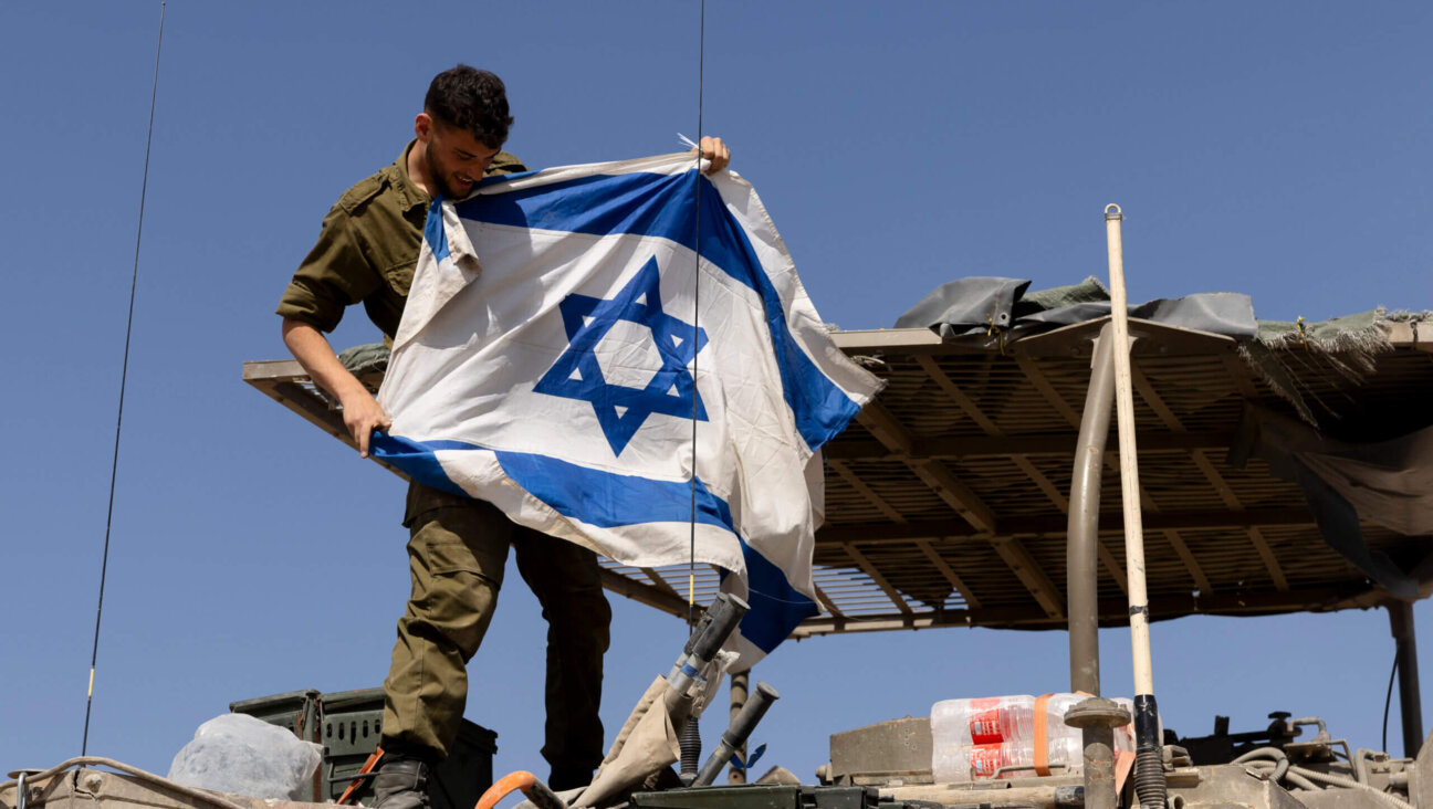 An Israeli soldier hangs an Israeli flag on an armored personnel carrier near the border with the Gaza Strip, April 15, 2024.