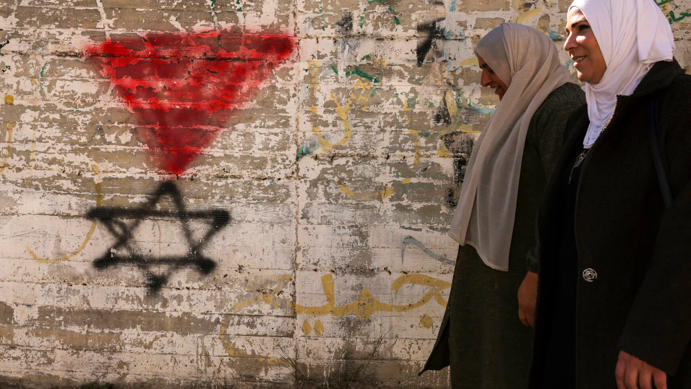 Palestinian women walk past a graffiti of the Star of David under an inverted "red triangle," a symbol that Hamas'  military wing, the Qassam Brigades, uses to identify Israeli targets in their videos, in the occupied West Bank city of Hebron on Nov. 30, 2023.