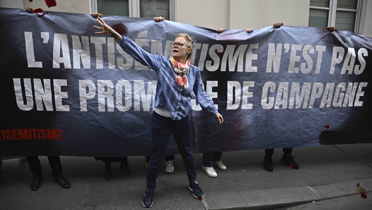 A member of the collective "Nous Vivrons"  a group fighting antisemitism, stands in front of a banner which reads "Antisemitism is not a campaign promise." 