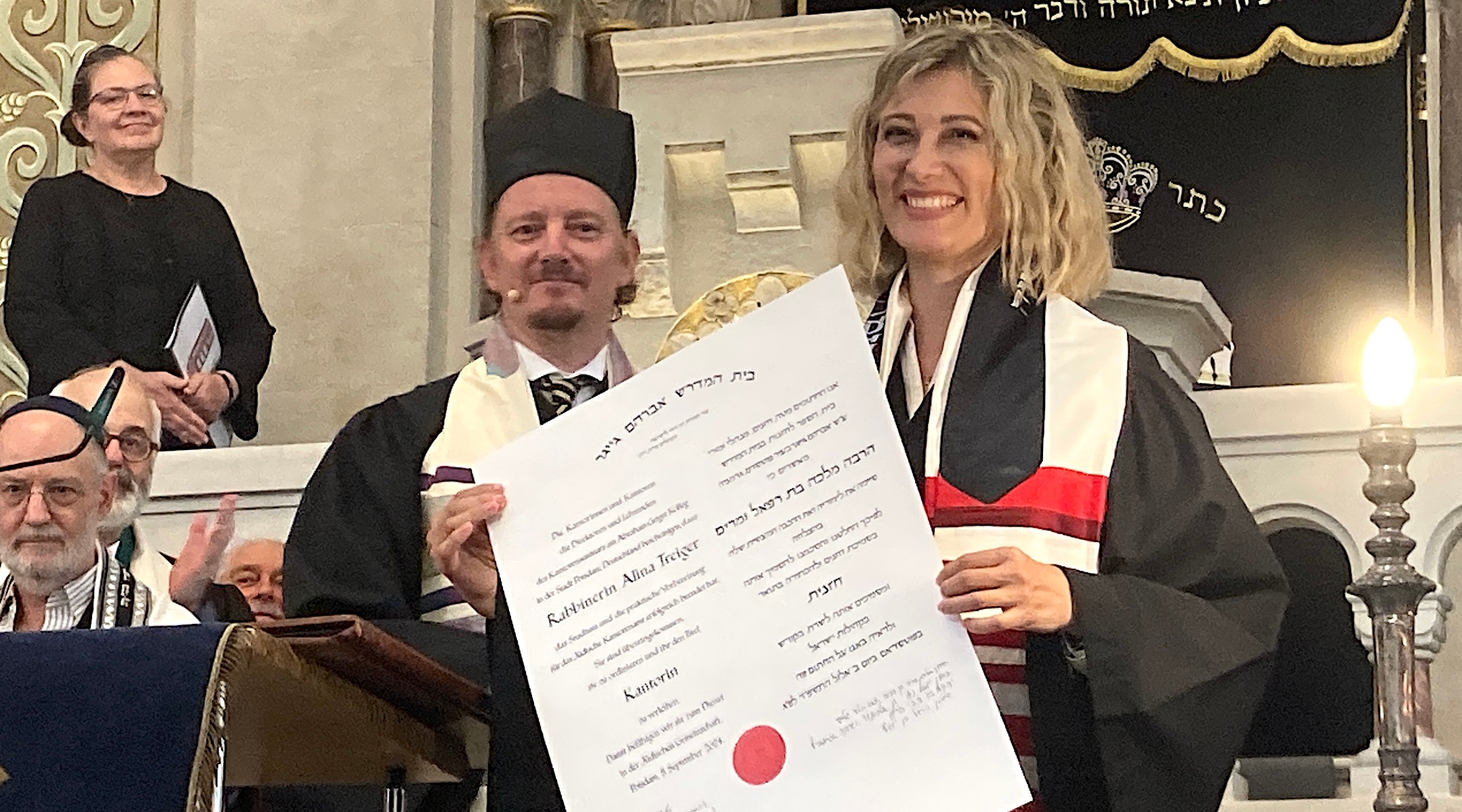 Cantor Shulamit Lubowska accepts her new certificate of ordination and a key to the Jewish community of Magdeburg at a ceremony at Berlin’s Rykestrasse synagogue, Sept. 5, 2024. Cantor Isidoro Abramowicz is at left. (Toby Axelrod).