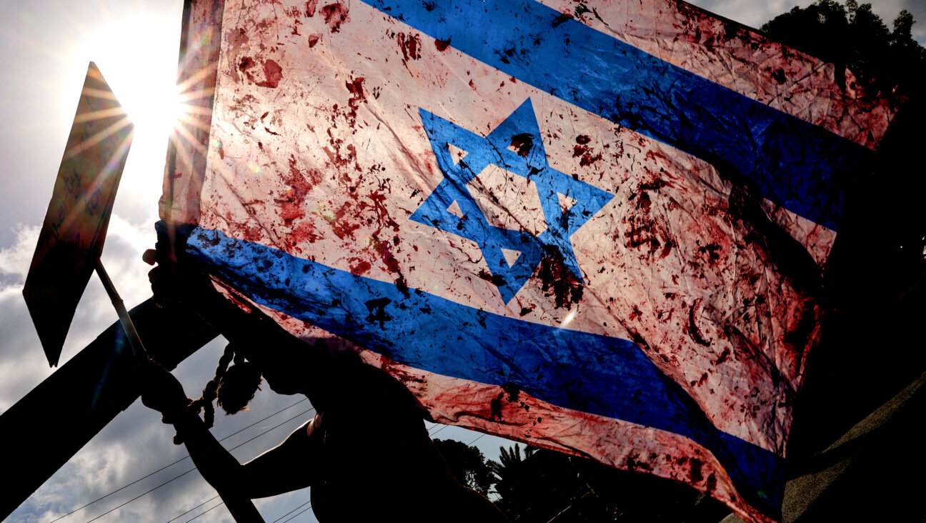 A demonstrator raises an Israeli national flag smeared with red paint as others block traffic on a main road during an anti-government protest calling for the release of the remaining Israeli hostages.