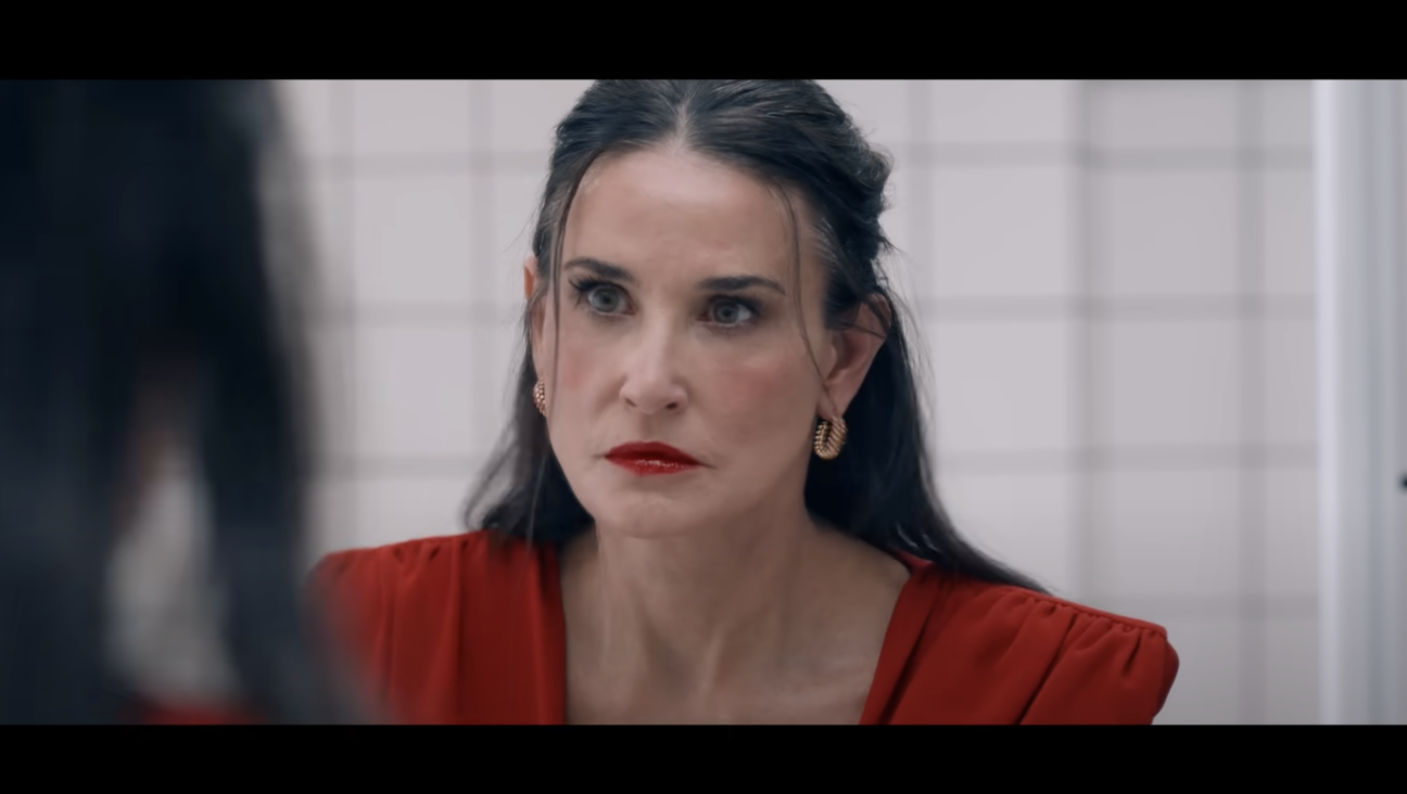 Actress Demi Moore stares at her reflection in the mirror in a YouTube screenshot from the trailer for <i>The Substance</i>