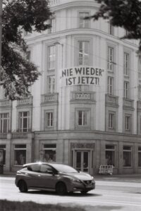 A banner that says "NIE WIEDER IST JETZT!" or "Never again is now!" hangs from a building.