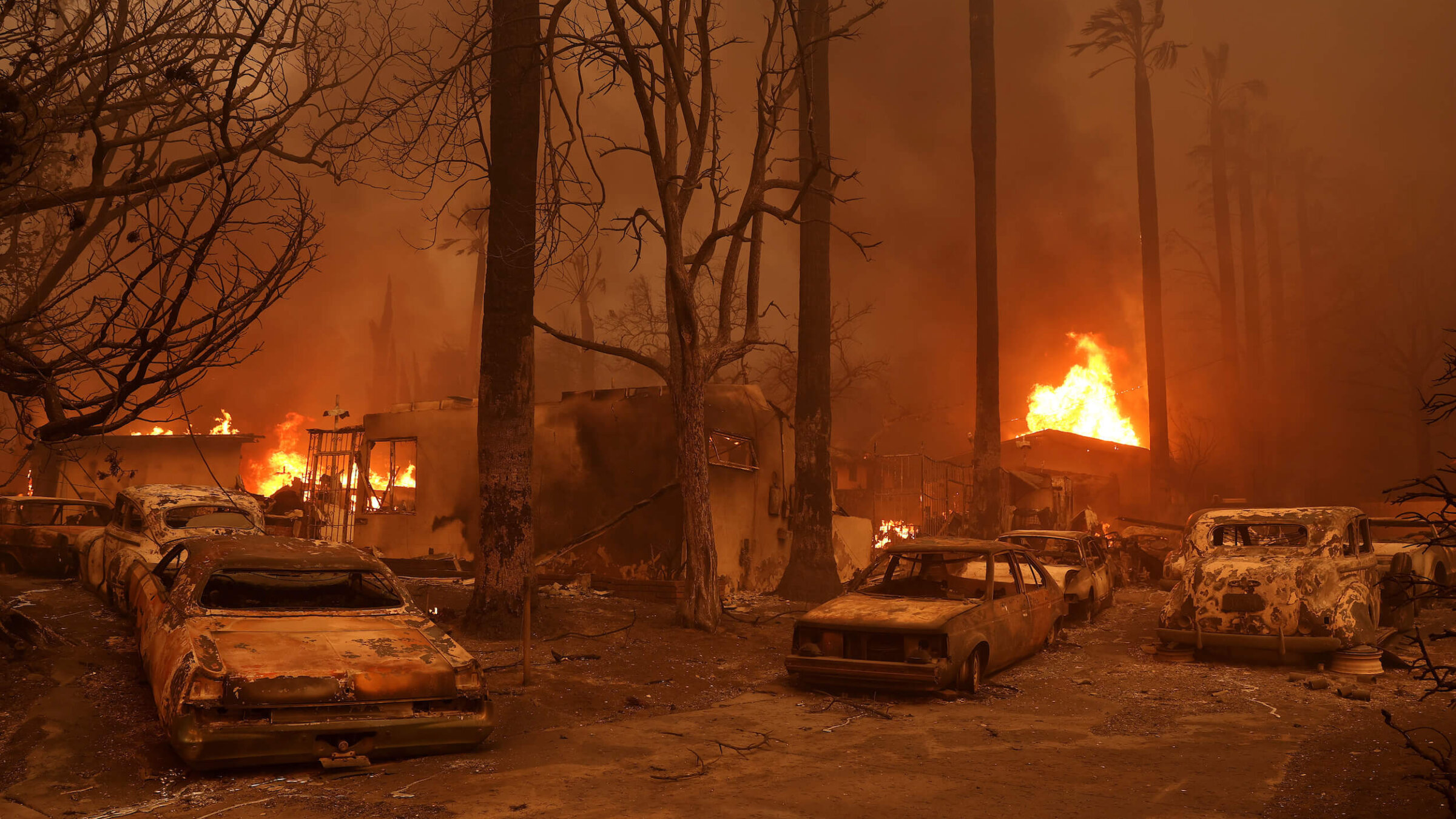 Burned cars sat parked in front of a burning home as the Eaton Fire moved through Altadena, California, on Wednesday.