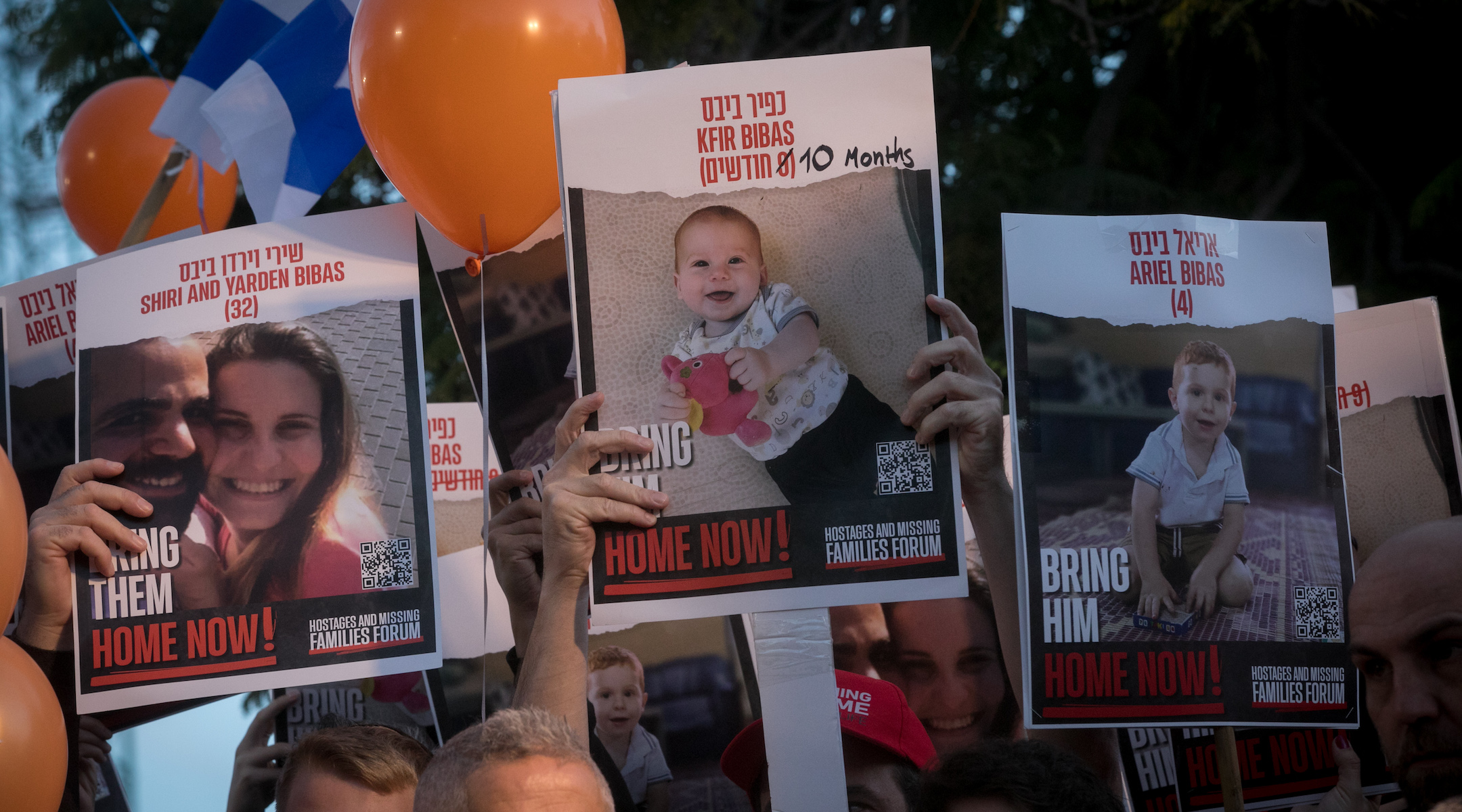 Israelis hold photographs of Shiri, Kfir and Ariel Bibas at a gathering calling for their release at Hostage Square in Tel Aviv, on November 28, 2023. (Miriam Alster/Flash90)