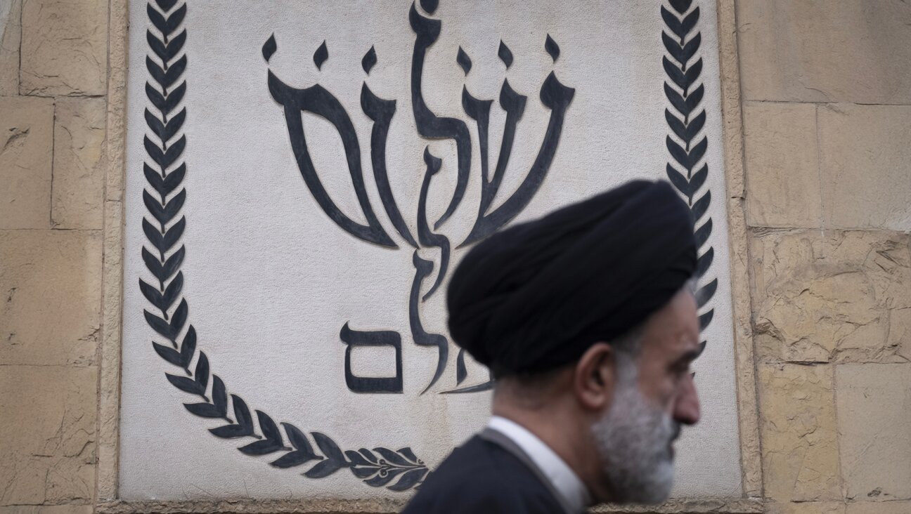 An Iranian cleric walks past a Jewish symbol of a menorah, shaped to spell the Hebrew words “shalom olam,” meaning “world peace,” during a ceremony commemorating the Jewish soldiers who died in the Iran-Iraq war (1980-88) at a Jewish cemetery in southern Tehran, Iran, on Feb. 6, 2025. (Morteza Nikoubazl/NurPhoto via Getty Images)