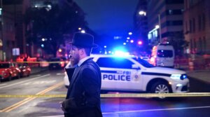 A man, standing behind police tape, talks on his cell phone outside the Capital Jewish Museum following a shooting that left two people dead, in Washington, DC, in the early hours of May 22, 2025. Two Israeli embassy staffers were killed in the shooting. (Alex Wroblewski/AFP via Getty Images)