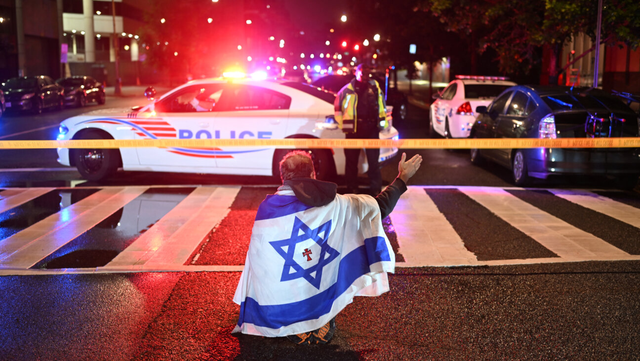 A man draped in the Israeli flag, bearing a cross and the name "Jesus" at its center, gestures as Metropolitan Police officers secure the area outside the Capital Jewish Museum following a shooting that left two people dead in Washington, DC, in the early hours of May 22, 2025. Two Israeli embassy staffers were shot dead late Wednesday, May 21, outside a Jewish museum in Washington by a gunman who shouted "free Palestine," authorities said, with US officials and Israeli diplomats expressing shock and outrage over the killings. (Photo by Alex WROBLEWSKI / AFP) (Photo by ALEX WROBLEWSKI/AFP via Getty Images)