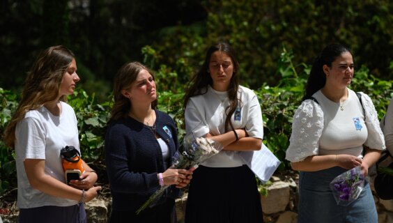 ישׂראלס יוגנט בײַ די קבֿרים פֿון אומגעקומענע פֿרײַנד אין הר הרצל: טראַדיציאָנעל געקליידטע אין בלוי־ווײַס, מיטן יזכּור־קוויטל