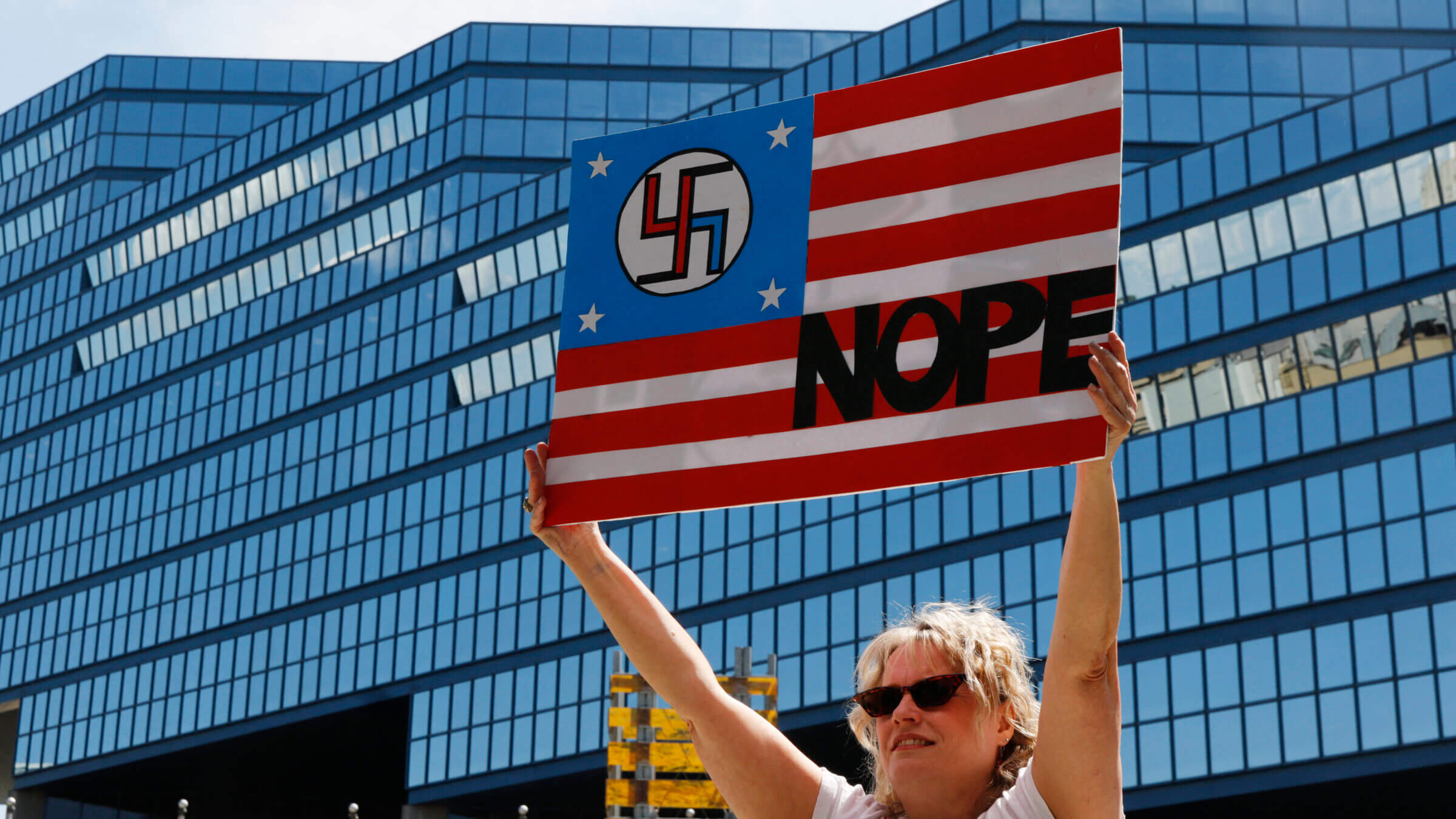 A person holds up a sign in the colors of the American flag with a swastika.