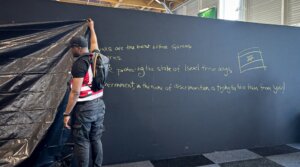 A security personnel works to hide a graffiti reading “Behind these walls are the best defense systems used by many countries. These systems are protecting the state of Israel these days. The French government, in the name of discrimination is trying to hide them from you!”, on a panel of the Israel Aerospace Industries (IAI) Israeli Pavillon during the International Paris Air Show at the Le Bourget Airport on June 16, 2025. (Mathieu RABECHAULT/AFP)