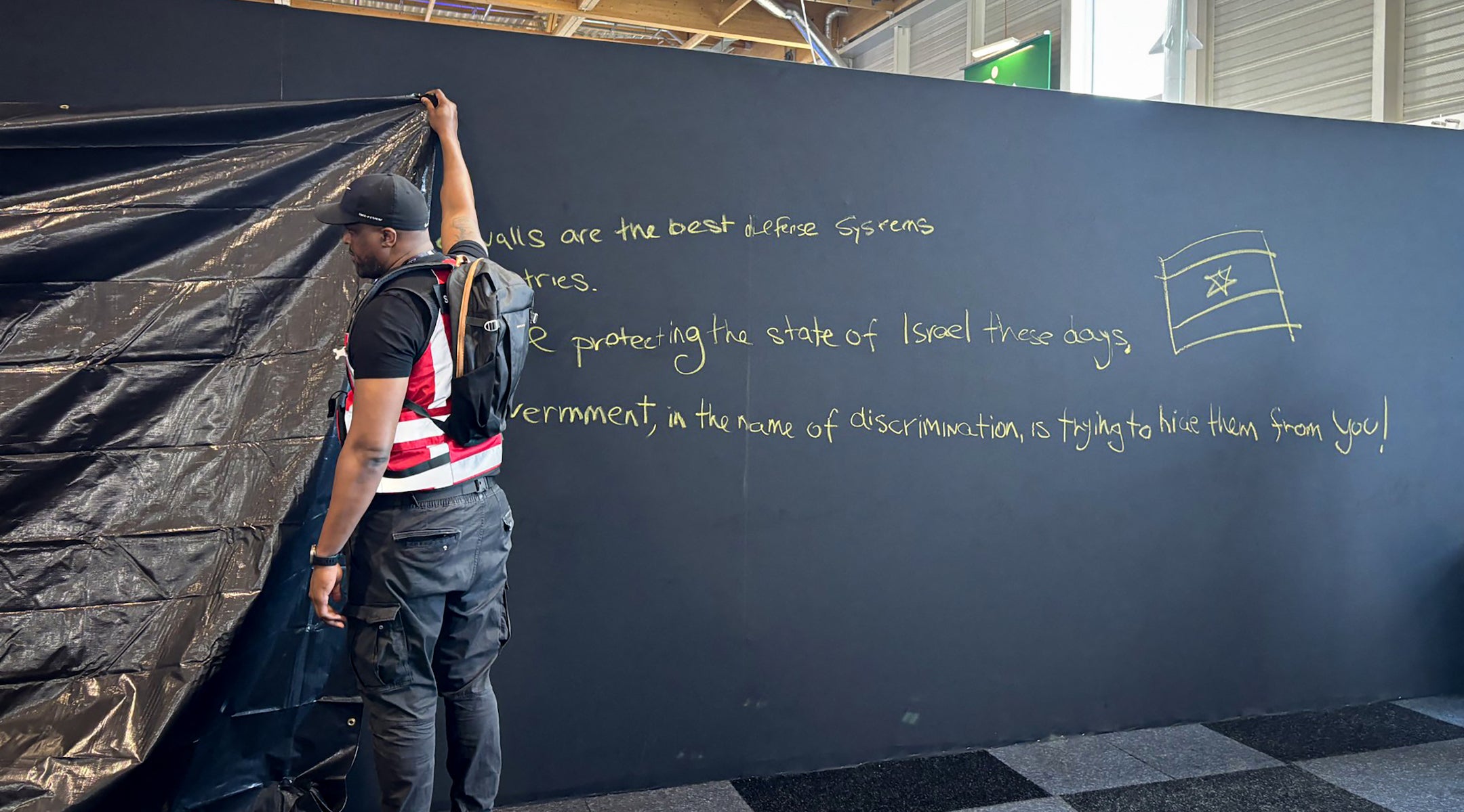 A security personnel works to hide a graffiti reading “Behind these walls are the best defense systems used by many countries. These systems are protecting the state of Israel these days. The French government, in the name of discrimination is trying to hide them from you!”, on a panel of the Israel Aerospace Industries (IAI) Israeli Pavillon during the International Paris Air Show at the Le Bourget Airport on June 16, 2025. (Mathieu RABECHAULT/AFP)