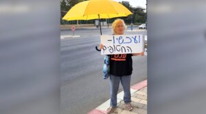 Naomi Shaanan, killed when an Iranian missile struck her apartment building in Beersheba on June 24, 2025, holds a sign in Hebrew that reads, “And now — the hostages.” 