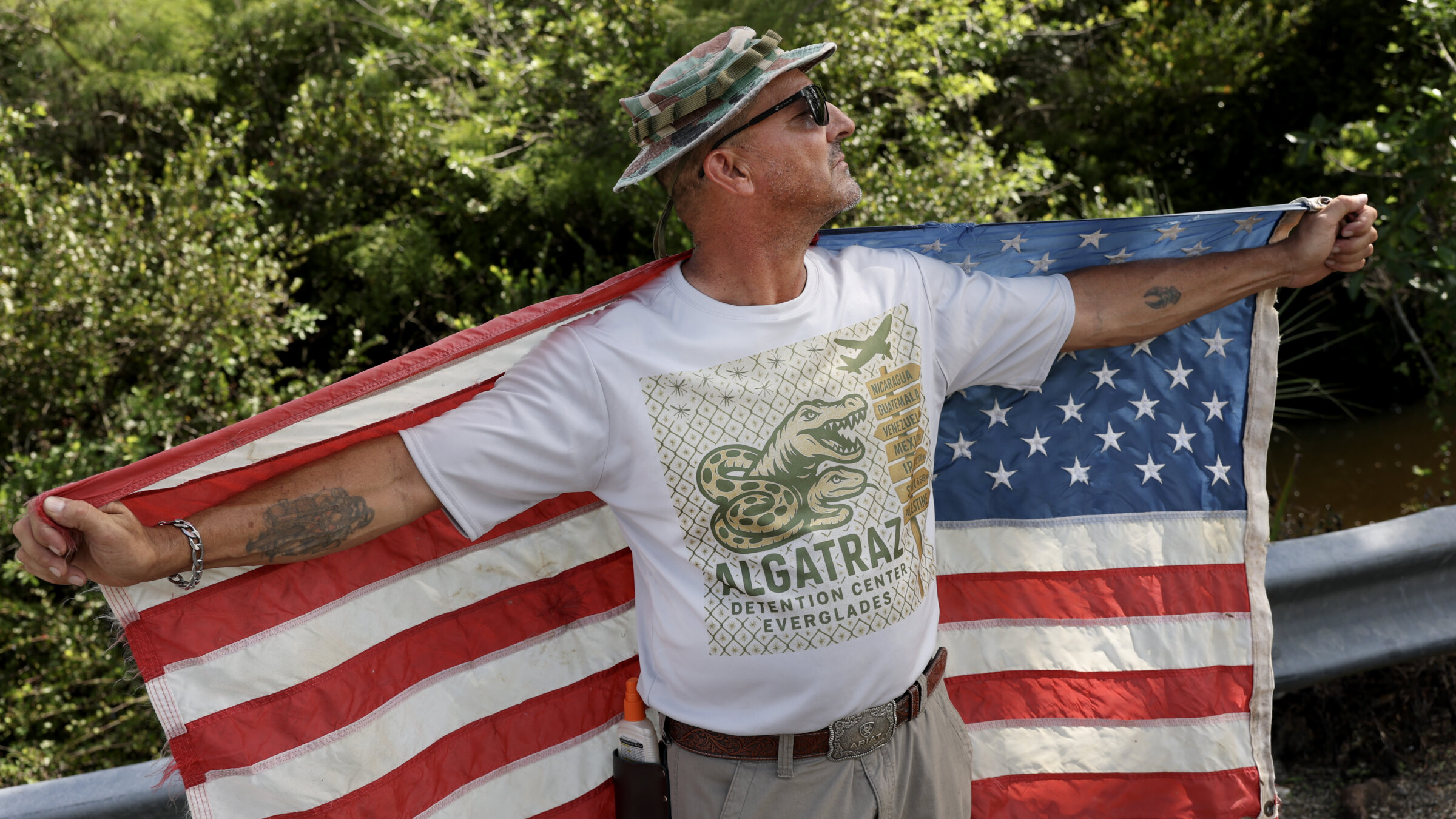 Marc Ribas holds a flag and wears independently produced merchandise advertising "Alligator Alcatraz," the new state-managed immigrant detention facility in Ochopee, Florida, on July 12.  