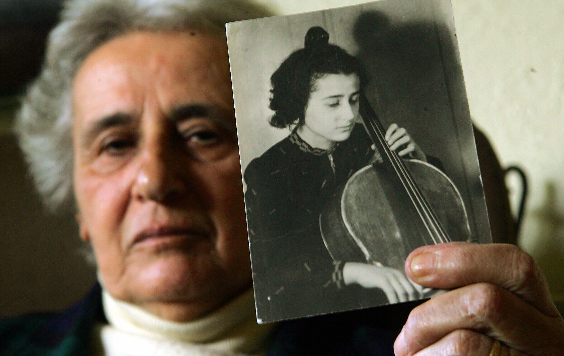 Holocaust survivor Anita Lasuer holds up a portrait of herself playing the cello. She survived Aucshwitz in part, because she played in the orchestra.   