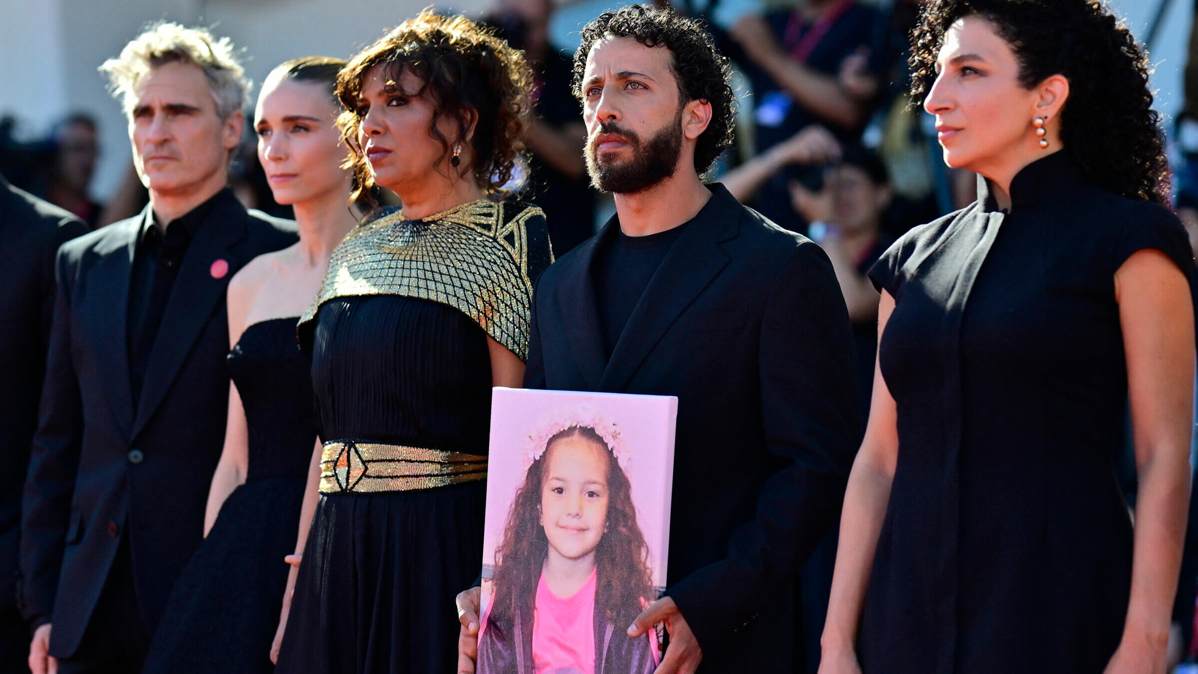 From left: Joaquin Phoenix, Rooney Mara, Kaouther Ben Hania, Motaz Malhees and Clara Khoury pose with a portrait of late Palestinian girl Hind Rajab during the red carpet for the movie "The Voice of Hind Rajab" presented in competition at the 82nd International Venice Film Festival.