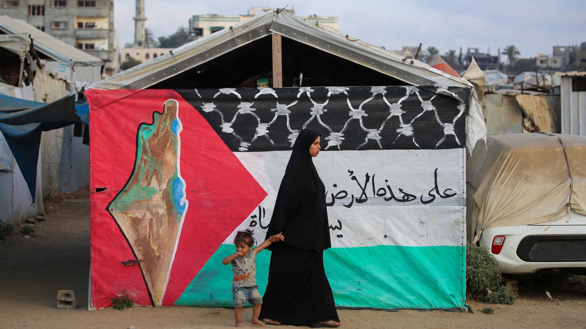 A Palestinian woman walks with a child past a Palestinian flag at the Bureij camp for refugees in the central Gaza Strip on Sept. 22.