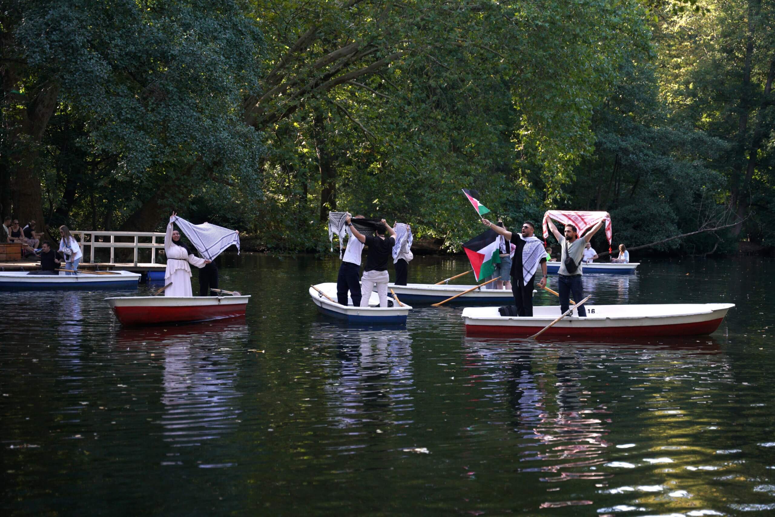 People in row boats hold of keffiyehs and Palestinian flags