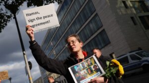 A woman holds a placard that reads: “Hamas, sign the peace agreement!” while holding photographs of German citizens who are among the hostages still being held by Hamas in Gaza during a demonstration outside the Foreign Ministry on Oct. 2, 2025, in Berlin. 