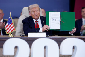 President Donald Trump holds up a signed Gaza ceasefire agreement at a summit in Egypt. 