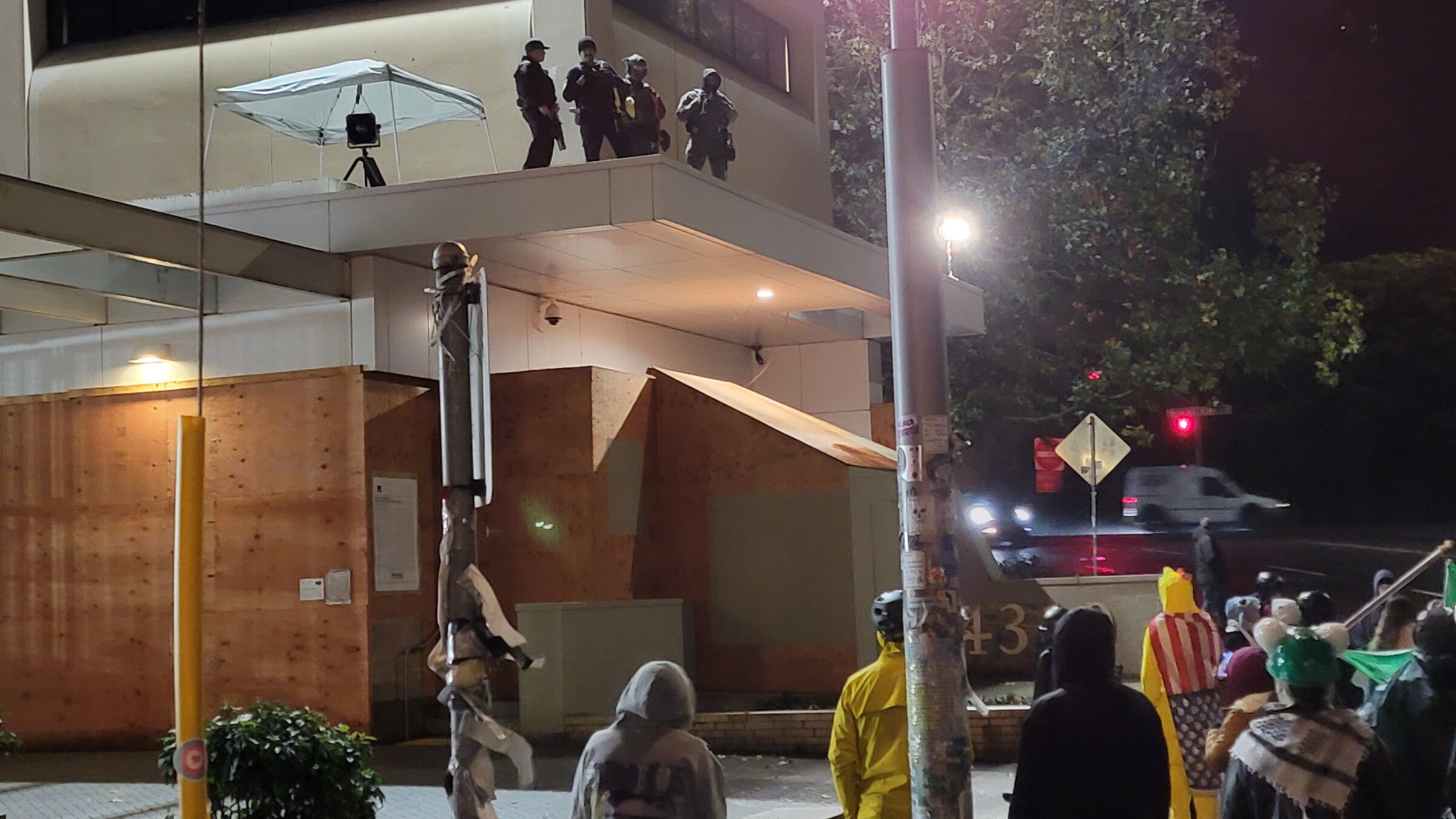 אַ גרופּע פֿעדעראַלע „אײַס“־אַגענטן, אױפֿן דאַך פֿונעם „אײַס“־בנין אין פּאָרטלאַנד, אָרעגאָן, וואַכן איבער אַ גרופּע דעמאָנטסראַנטן אין פּאָרטלאַנד, אָרעגאַן, דעם 25סטן אָקטאָבער