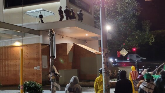 אַ גרופּע פֿעדעראַלע „אײַס“־אַגענטן, אױפֿן דאַך פֿונעם „אײַס“־בנין אין פּאָרטלאַנד, אָרעגאָן, וואַכן איבער אַ גרופּע דעמאָנטסראַנטן, דעם 25סטן אָקטאָבער 

