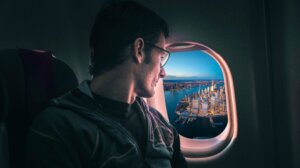 A man stares down at New York City as his airplane leaves. 