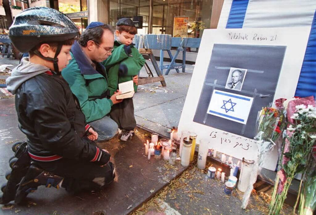 Robert Marx leads his sons Joshua and Benjamin in prayer next to a makeshift memorial to Israeli Prime Minister Yitzhak Rabin in front of the Israeli consulate in New York, on Nov. 5, 1995.                               (Photo by BOB STRONG / AFP) (Photo by BOB STRONG/AFP via Getty Images)