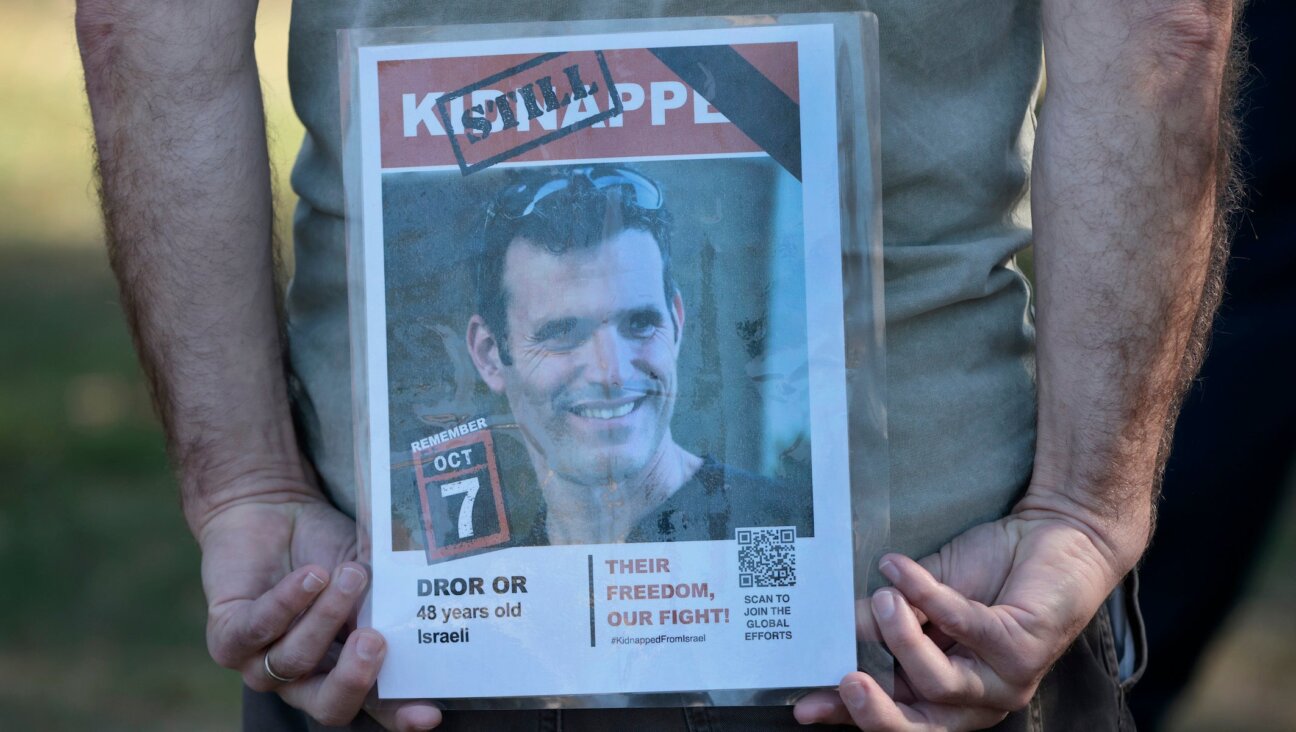 A member of Run for Their Lives holds a photo of Dror Or behind his back so it can be seen by people passing by the gathering in Newton Centre on October 5, 2025. 