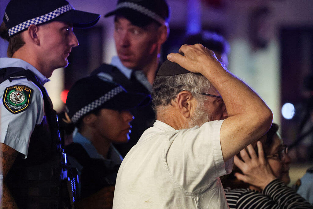 A member of the Jewish community reacts as he walks with police towards the scene of a shooting at Bondi Beach in Sydney on December 14, 2025.