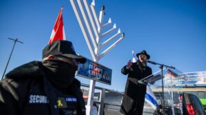 Flanked by private security, Rabbi Moshe Steiner speaks at a Hanukkah gathering in Toronto, Dec. 14.