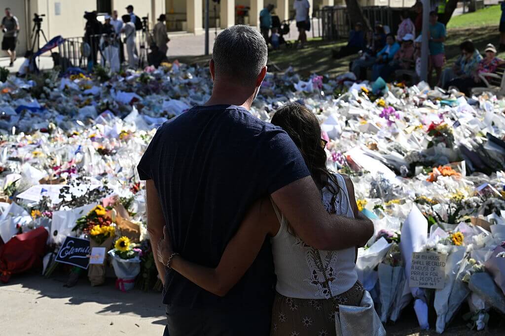 A couple hold one another as they stand in silence at the flower memorial beside Bondi Pavilion on December 17, 2025 in Sydney, Australia. country. 