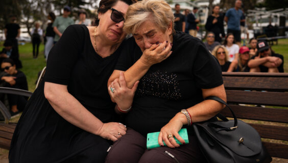 צוויי פֿרויען באַוויינען די קרבנות פֿונעם שיסערײַ אויף דער חנוכּה־מסיבה, לעבן דעם באָנדי־פּאַוויליאָן, אין סידני, אויסטאַרליע, דעם 16טן דעצעמבער
