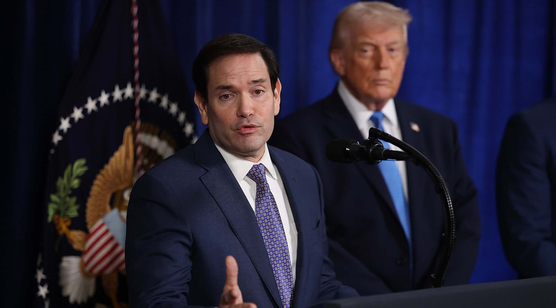 Secretary of State Marco Rubio speaks during a press conference as U.S. President Donald Trump listens at Mar-a-Lago club on January 03, 2026, in Palm Beach, Florida. During the event, President Trump confirmed that the U.S. military carried out a large-scale strike in Caracas overnight, resulting in the capture of Venezuelan leader Nicolas Maduro and his wife, Cilia Flores. 