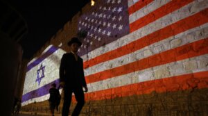 People walk past a projection depicting Israeli and US flags on the walls of Jerusalem’s Old City on Oct. 22, 2025.