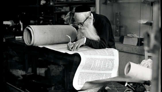Rabbi Eisenbach, Scribe, Lower East Side, 1975. Aron said the rabbi, who he had been spending time with, had refused to allow his photo to be taken. One day, Aron snapped the photo without asking and, when the rabbi looked over his glasses at the sound of the shutter, ran away. Later, he brought the print to show the scribe, who was delighted by it in the end.