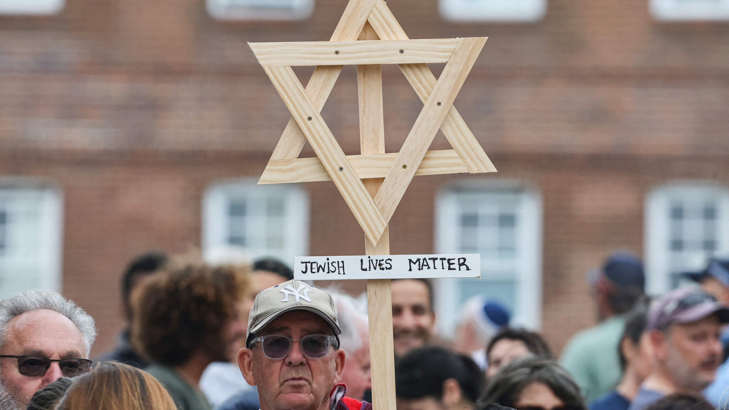 A mourner holds up a wooden Star of David with a sign reading "Jewish Lives Matter" as people gather around floral tributes outside Bondi Pavilion in Sydney, Australia on Dec. 16, 2025, to honour victims of the Bondi Beach shooting.